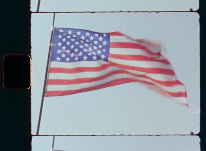 The US national flag is moving in the air on a windy and breezy fourth of July with bright sunshine and blue skies symbolizing the independence and freedom of the USA and the proud American spirit on old Super-8 film footage