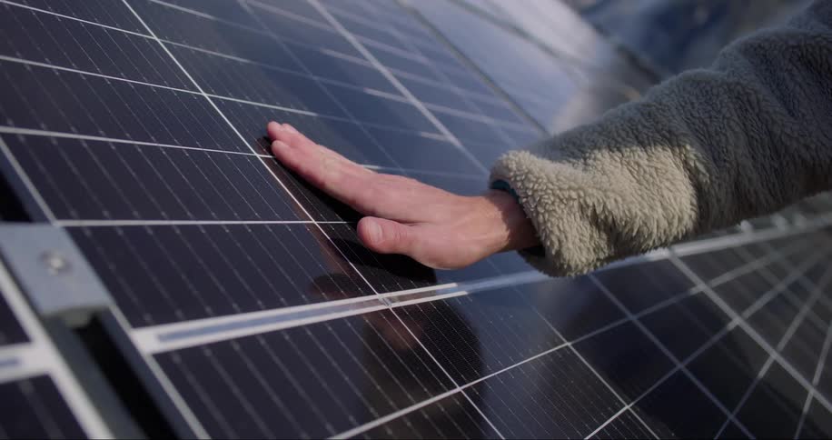A hand reaches to touch a solar panel