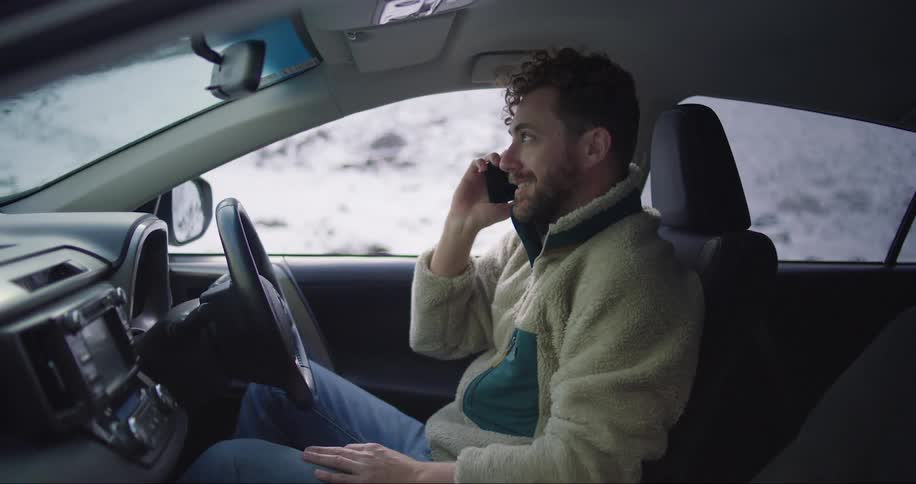 Happy man answers a call inside his car on the snowy countryside