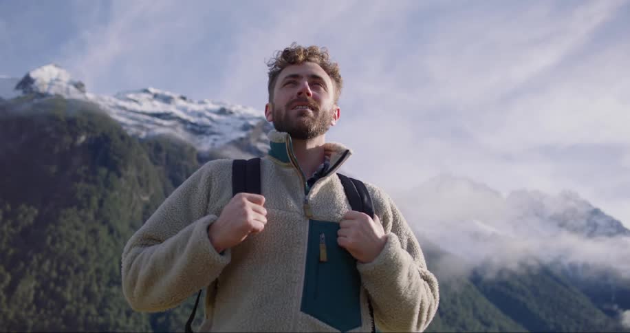 A man in a coat and backpack looking determinedly ahead in the middle of nature