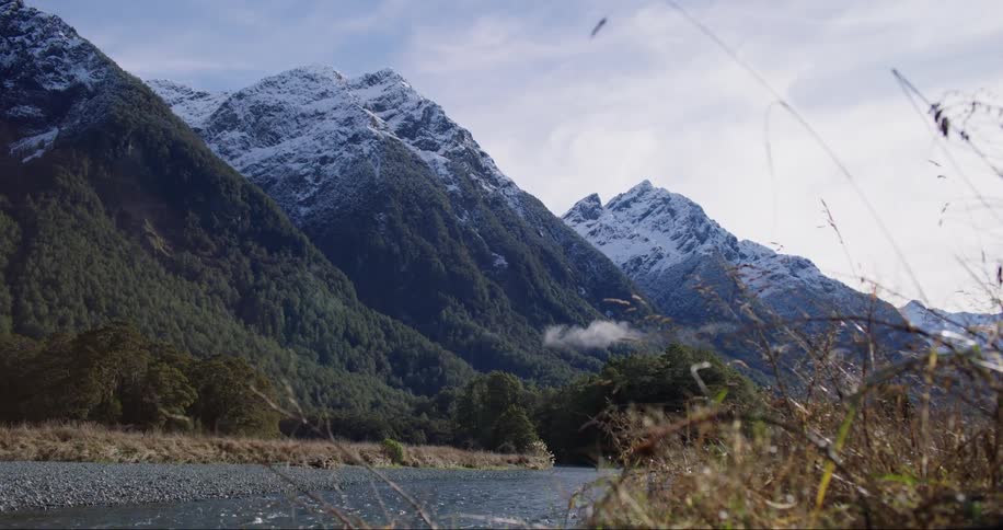 Broad river flows near the snow covered peaks of a mountain range