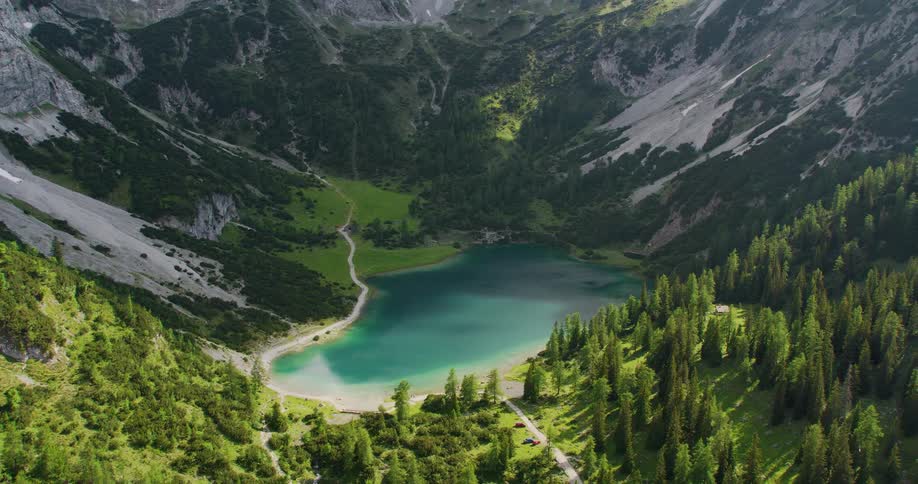 Aerial of a small lake surrounded by tall mountain peaks on a bright day
