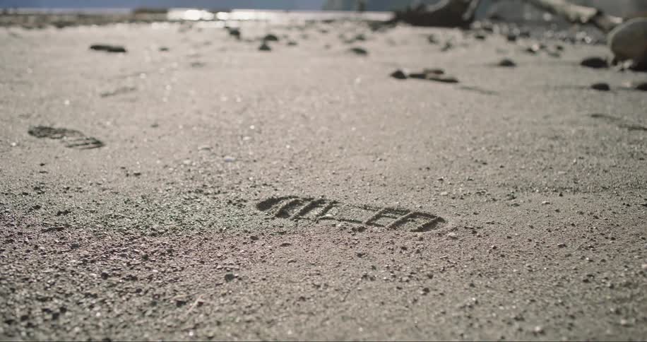 Person wearing boots and jeans leave footprints in the sand