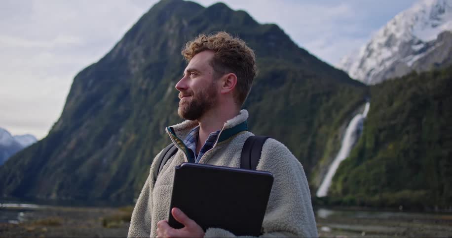 A man holding a laptop and wearing a backpack admires the canyon that hes standing in