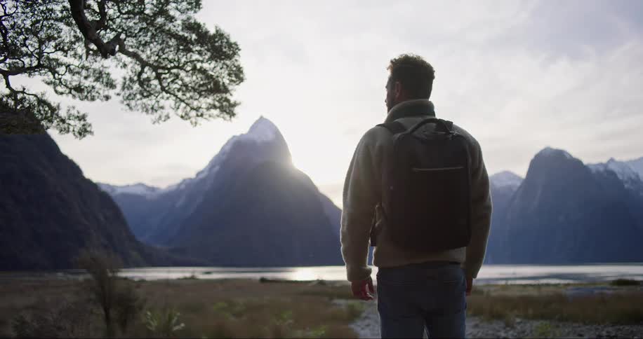 Man with a backpack on his back observing the lake and the snowcovered mountains around