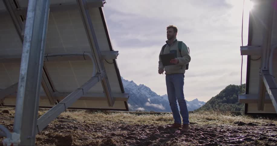 Man standing near solar panels in a mountain takes notes on a tablet