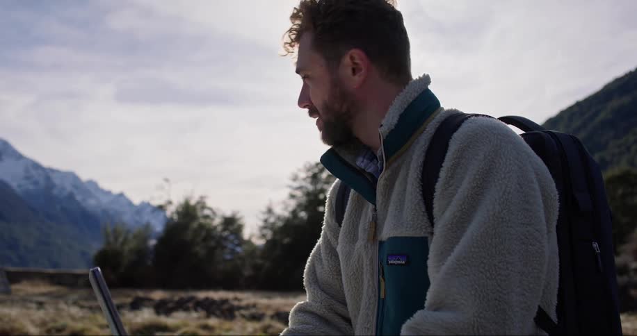 Man in the middle of nature with vegetation and icy mountains standing and typing on his portable notebook