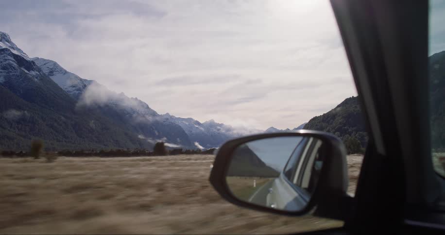 A car is traveling down a road near a mountain while the camera films the skyline