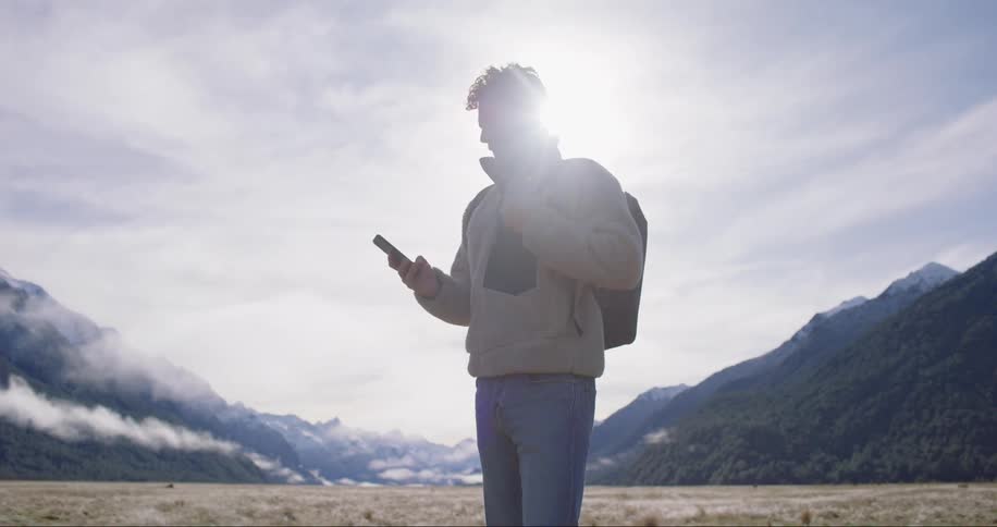 Man in nature surrounded by mountains points his cellphone and takes a photo