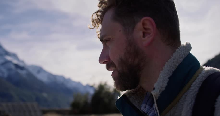 Face of a bearded young man standing near a mountain range