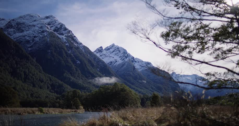 A road beside green hillsides in front of mountain with snow covered peak and sunset