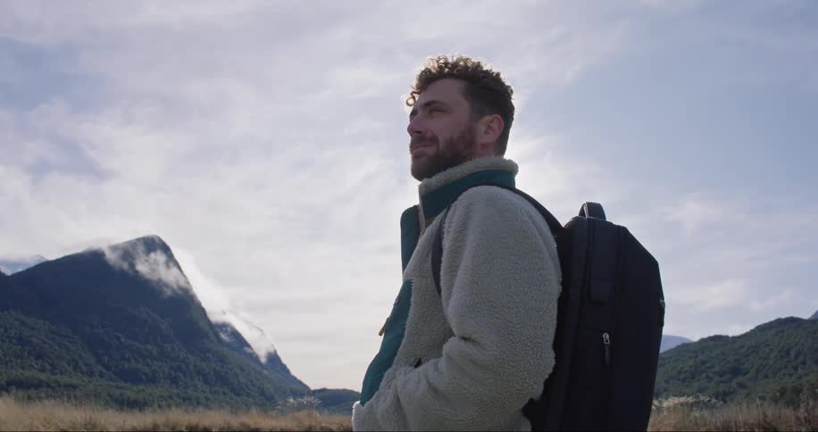 A man in a coat and backpack staring straight ahead in nature