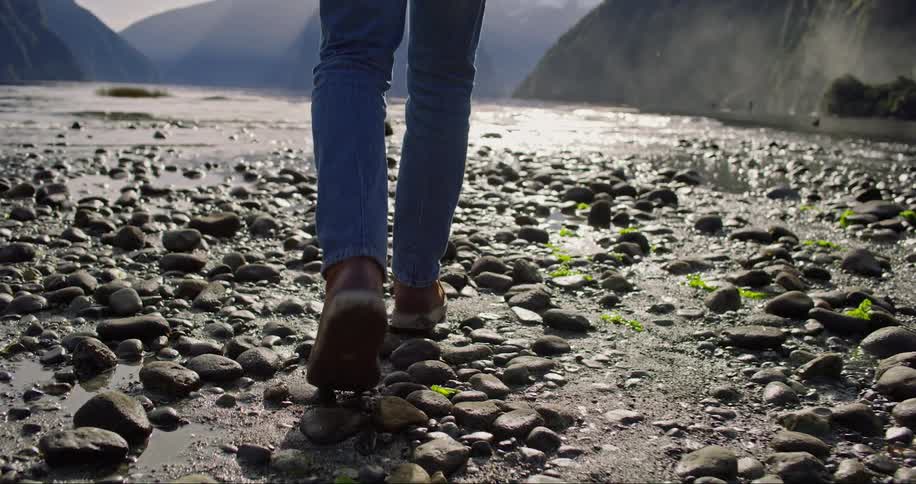 A person walks in slow motion along a muddy stream at the bottom of a rocky canyon