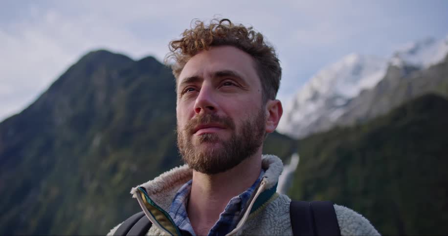 Close up of a mans face while he looks out in front of him taking in nature with tall mountains behind him