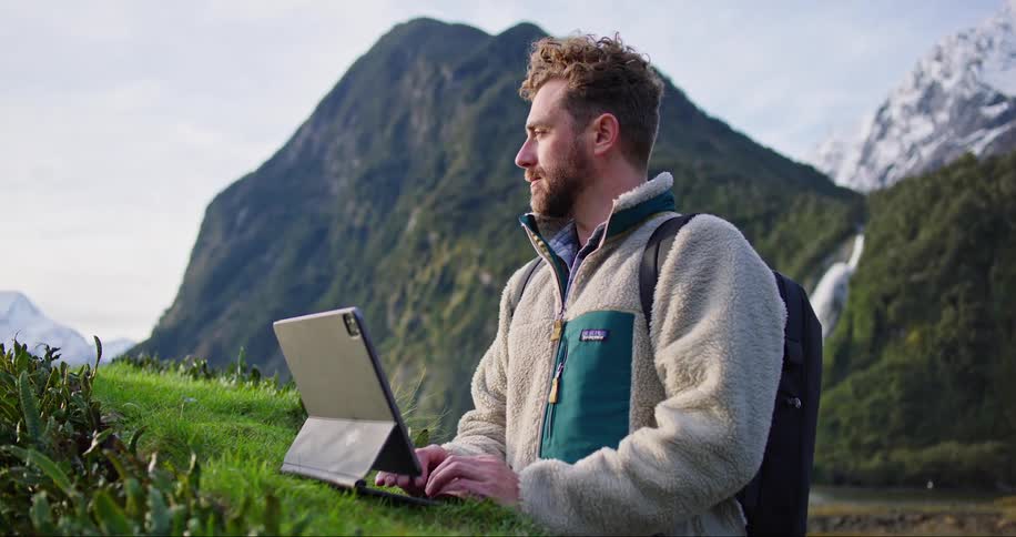 Man stands alone while typing on a computer with a mountain nearby
