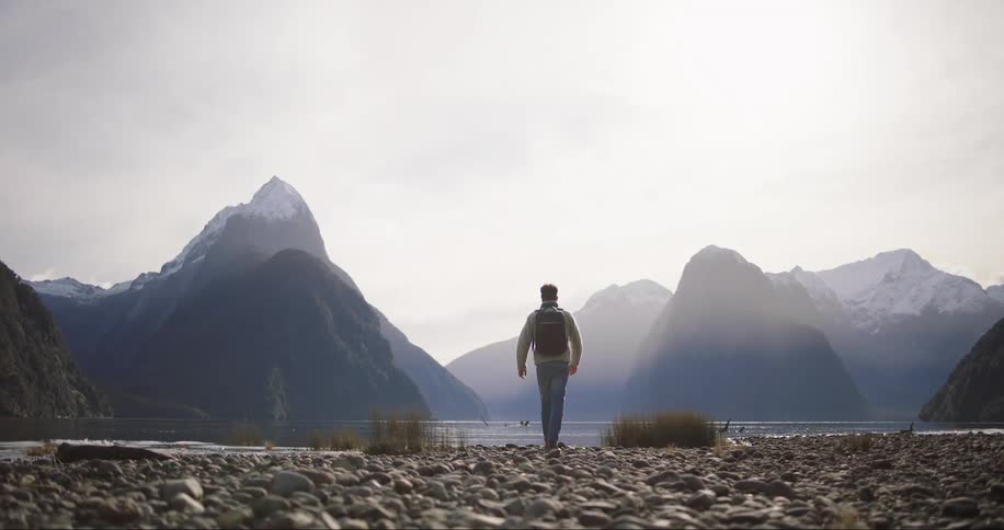 Man carrying a backpack stands on the shoreline of a lake in the mountains