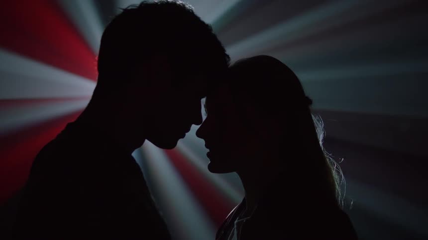 The silhouette of a couple of a man and a woman looking at each other passionately and in the background colored lights moving