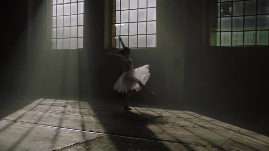 A woman in a skirt dancing ballet in an interior with only sunlight