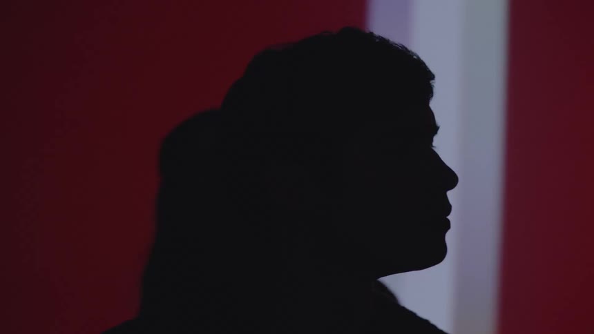 The silhouette of a man and woman looking sideways on a moving background of white and red colors