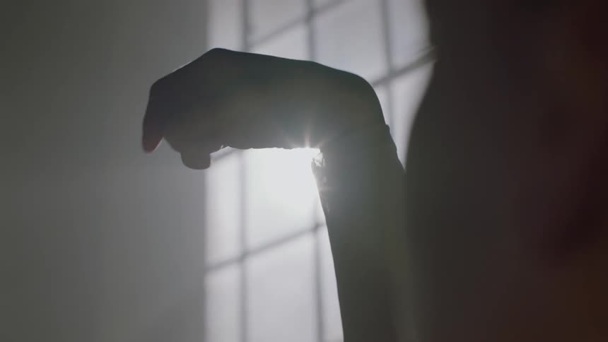 A dancer stands near a window and moves their hand