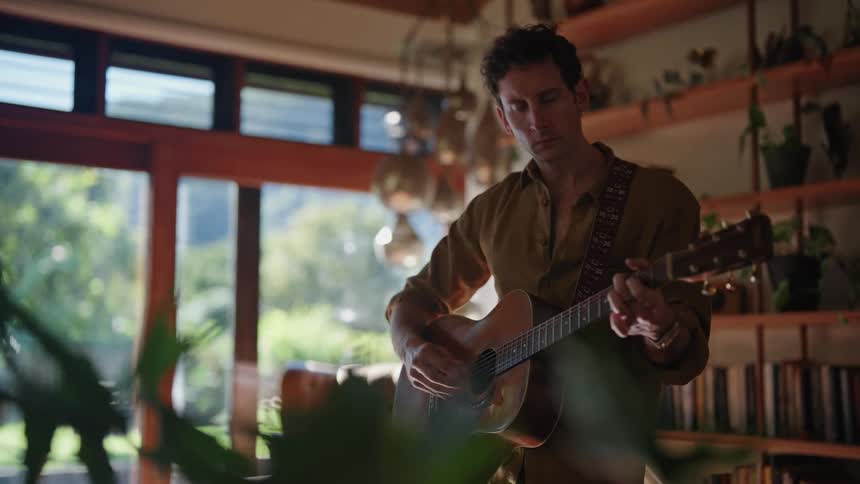 Young man plays acoustic guitar in the middle of the living room at home