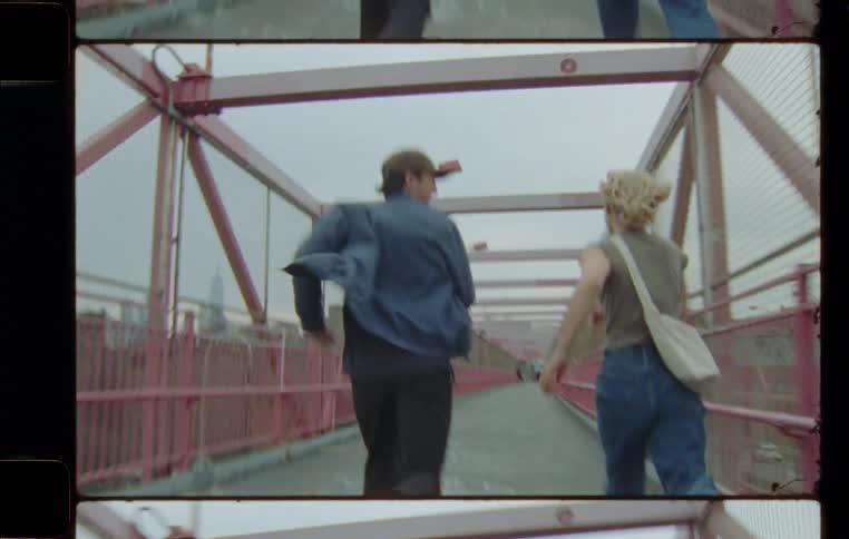 A man wearing a jacket and a woman carrying a bag running on a bridge while having fun