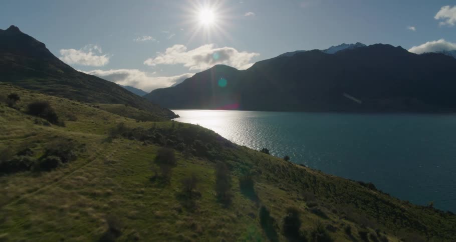 Aerial view of a mountain covered in vegetation next to a river with a man hiking on a path during day time