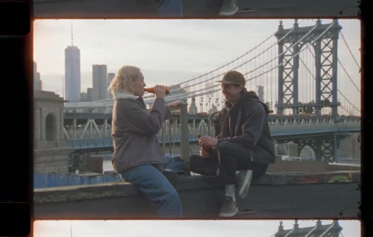 Two people drinking and talking sit on a wall in the city