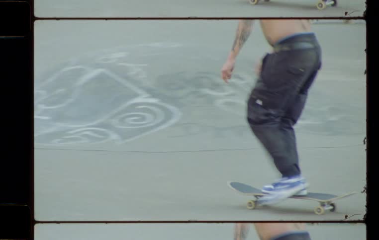 A shirtless man skateboards across concrete