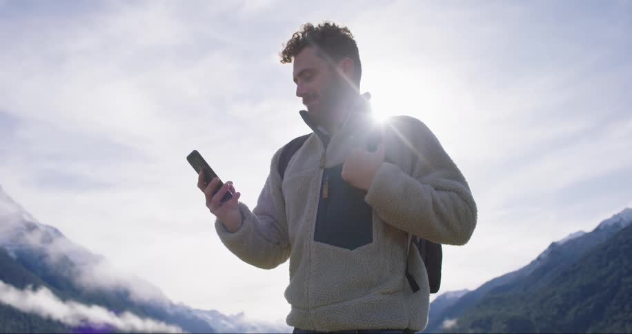 A man raises his phone to take a photo of the mountain range surrounding him
