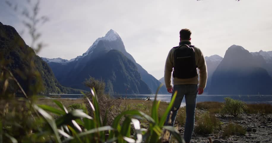 Hiker stands on field near lake looking over fog covered mountains