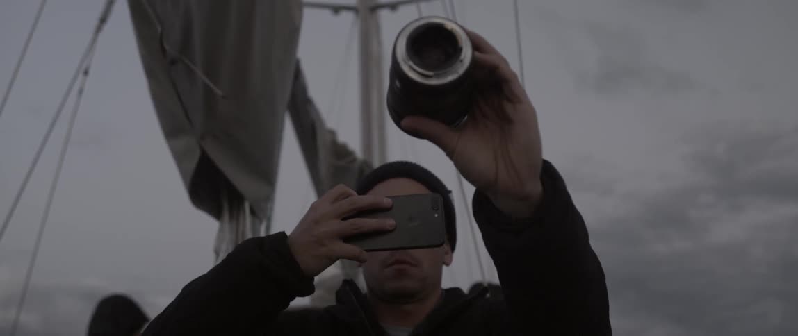 A man is taking a photograph on a boat with his phone and a telescope