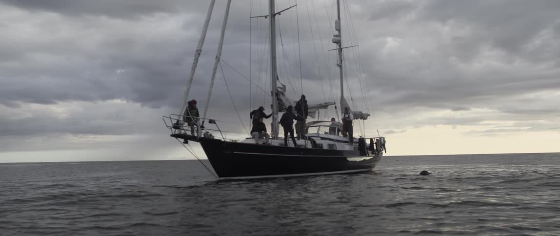 A person is swimming towards a boat on a cloudy day