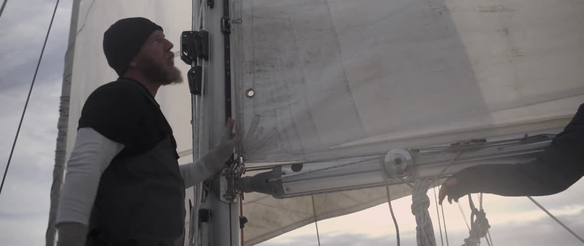 A man is talking and pointing towards parts of a sail