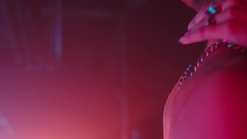 The neck and upper back of a shirtless man dancing as a womans hand reaches to touch his neck