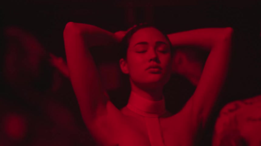 A young woman dancing in an indoor environment with low lighting and nightclub lights