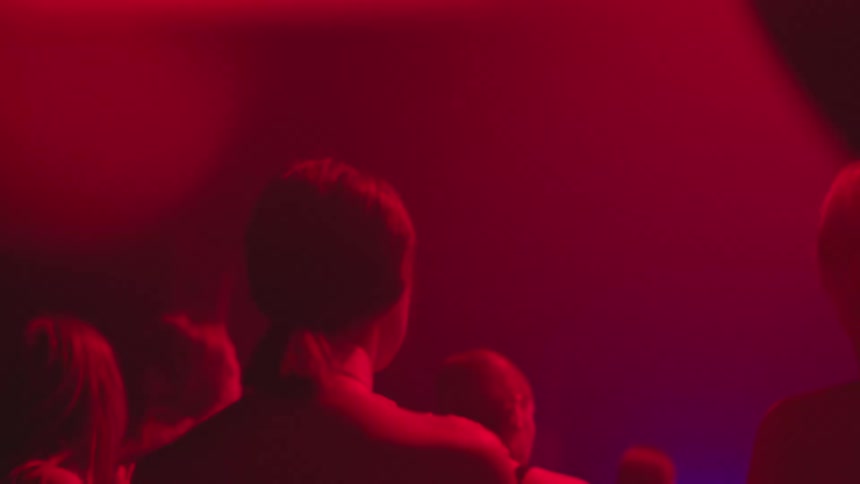 A woman is dancing in a nightclub surrounded by other people under the dim and flickering red lights