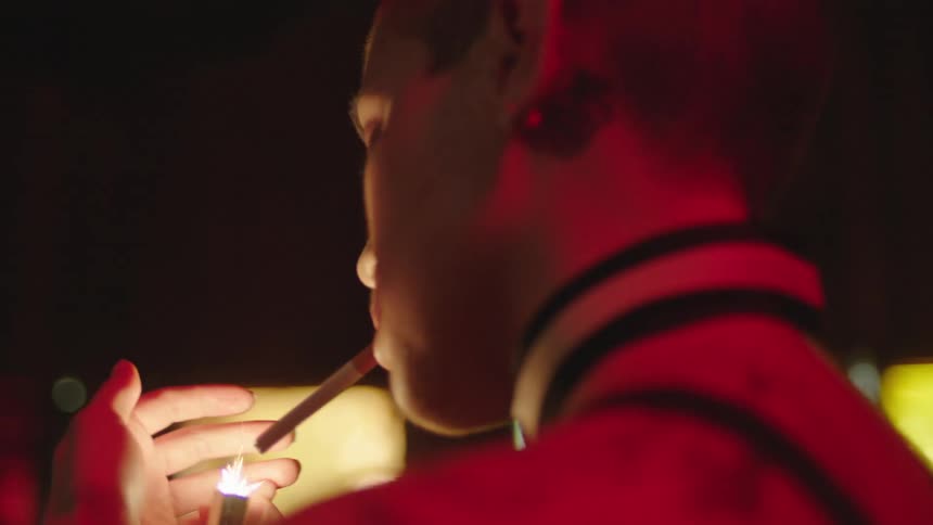 A young woman lighting a cigarette in a low lit environment
