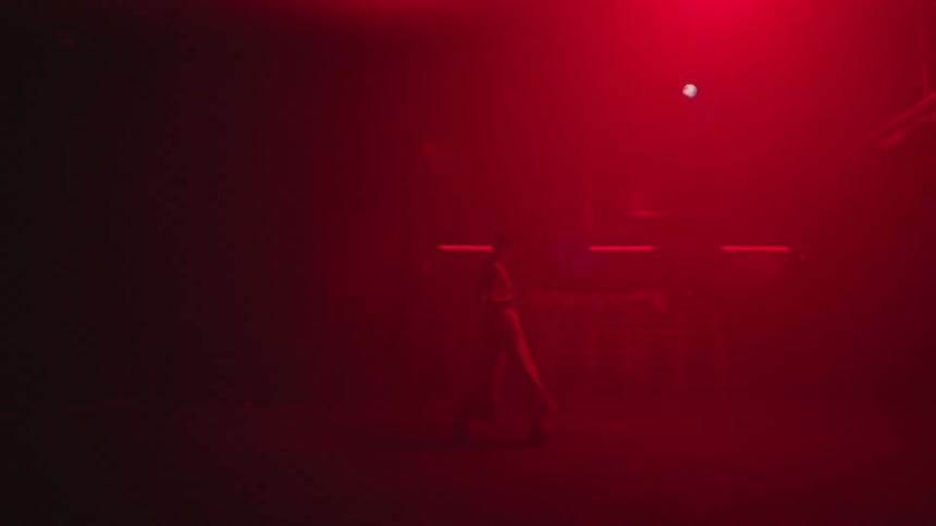 Silhouette of a person dancing on an open floor with bright white lights flashing with red lights on the wall