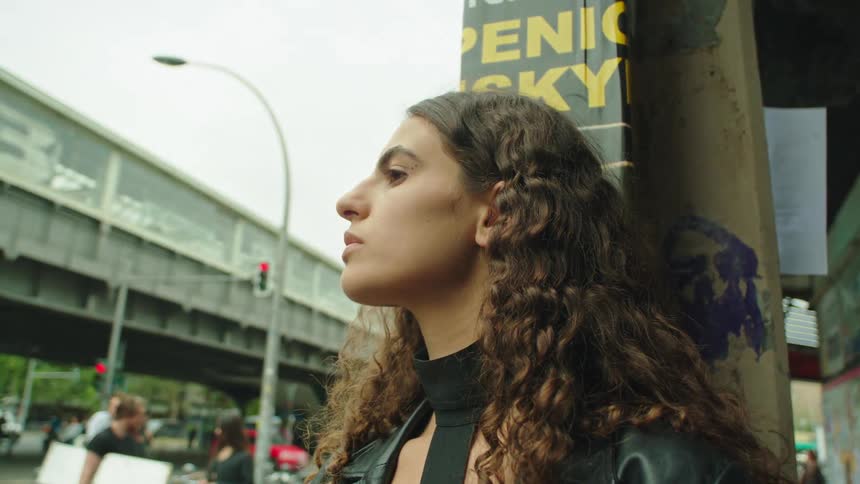 Woman wearing a black leather jacket stands on a street corner in the city