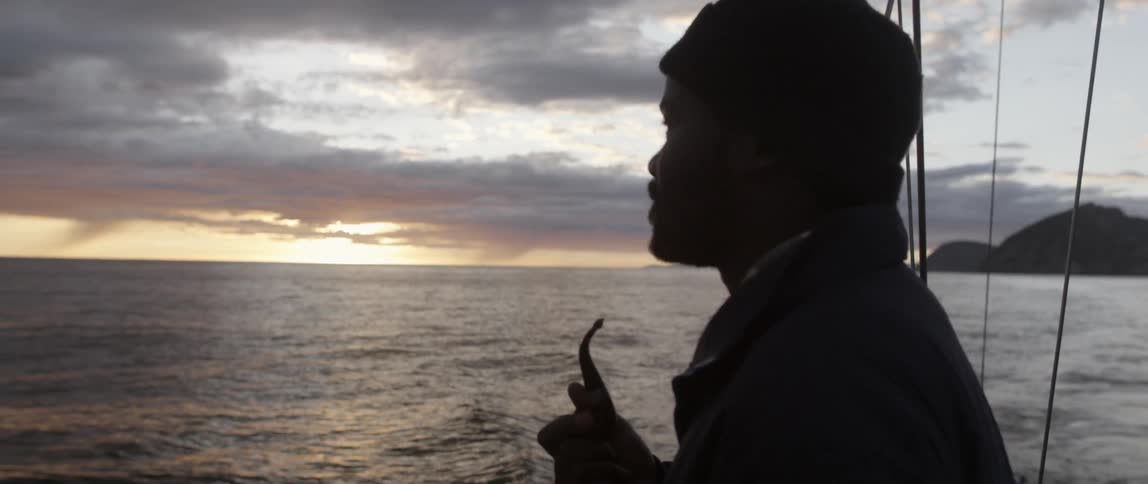 A man is smoking a pipe on a ship watching the sun set