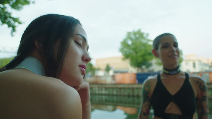 Woman with tattoos glances at her friend with eyes closed daydreaming outdoors