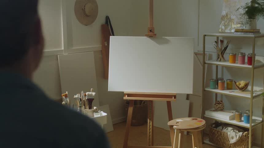 A man with his back turned walking backwards and observing a white painting canvas