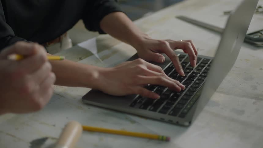 Closeup of hands typing on a laptop and another hand holding a pencil and gesturing