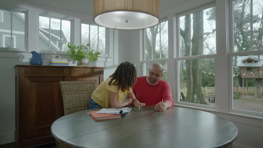 A man and a woman sitting at a table discuss what theyre seeing on a tablet