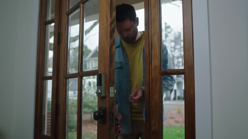 A man opens a glass door of a house and looks inside looking for something