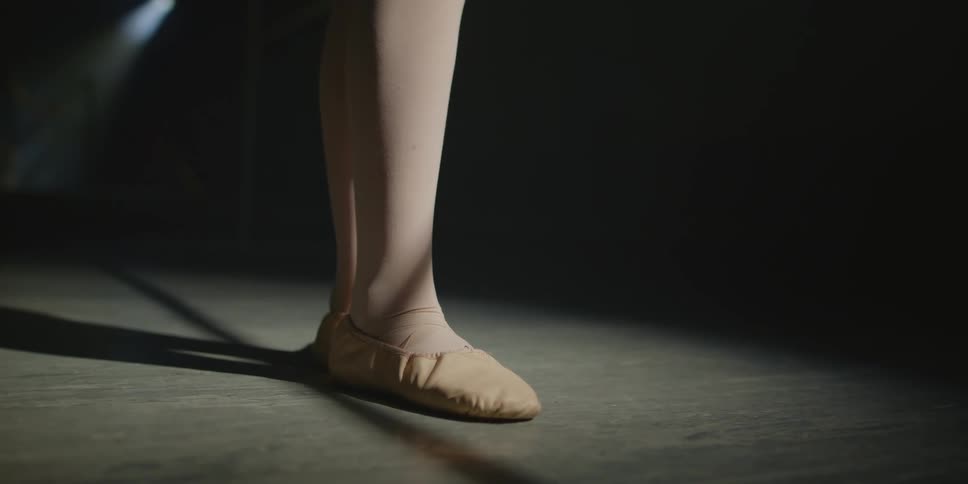 Close up of a persons feet in ballerina shoes up on tip toes on a hard floor