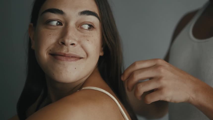 A woman looks affectionately at her partner's hands as he plays with her hair