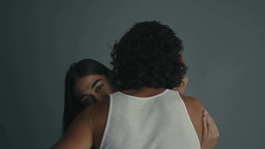 Woman sitting down hugging a man and caressing his back indoors