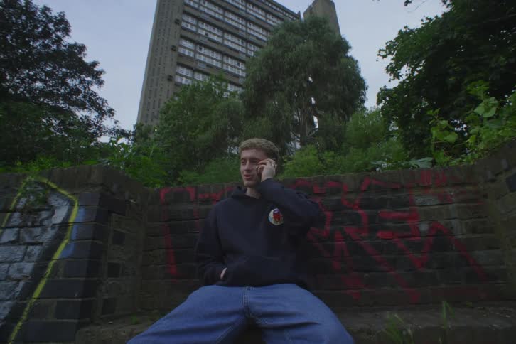 Man sits on bench near graffiti covered walls and talks on smartphone